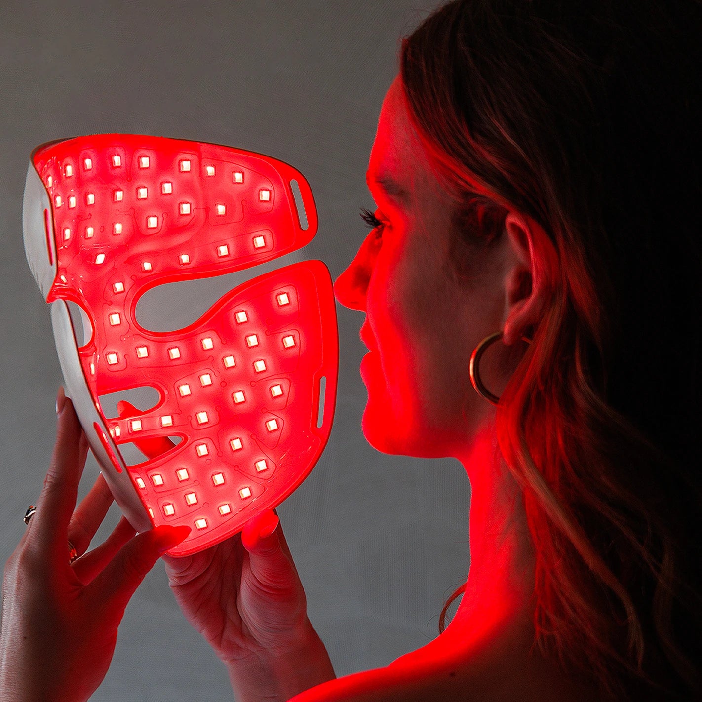 Person holding a red LED light therapy mask.