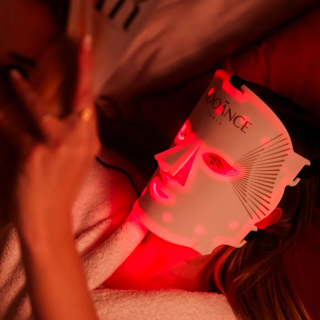 Person wearing a glowing LED face mask, lying down and holding a book.